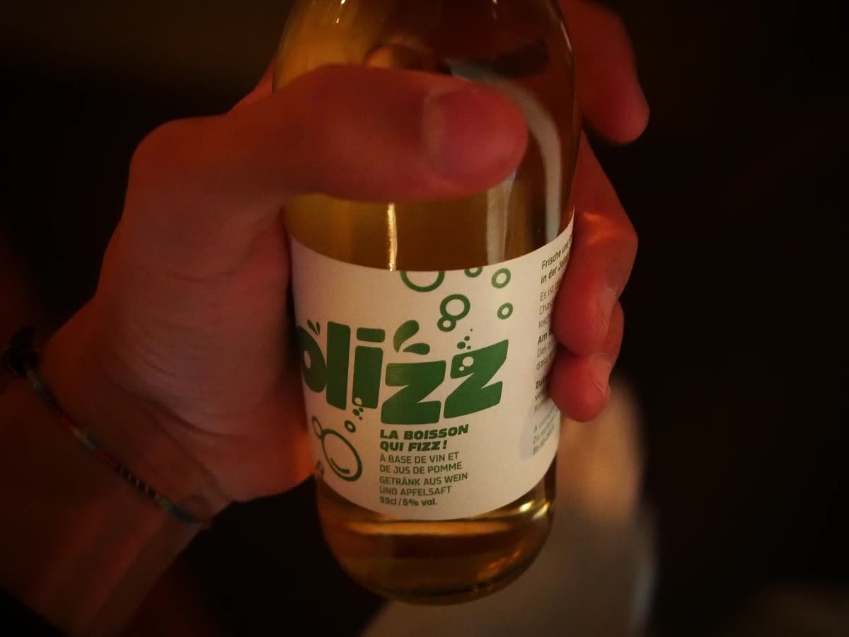 Eine Hand hält eine Flasche Plizz in warmem Licht.